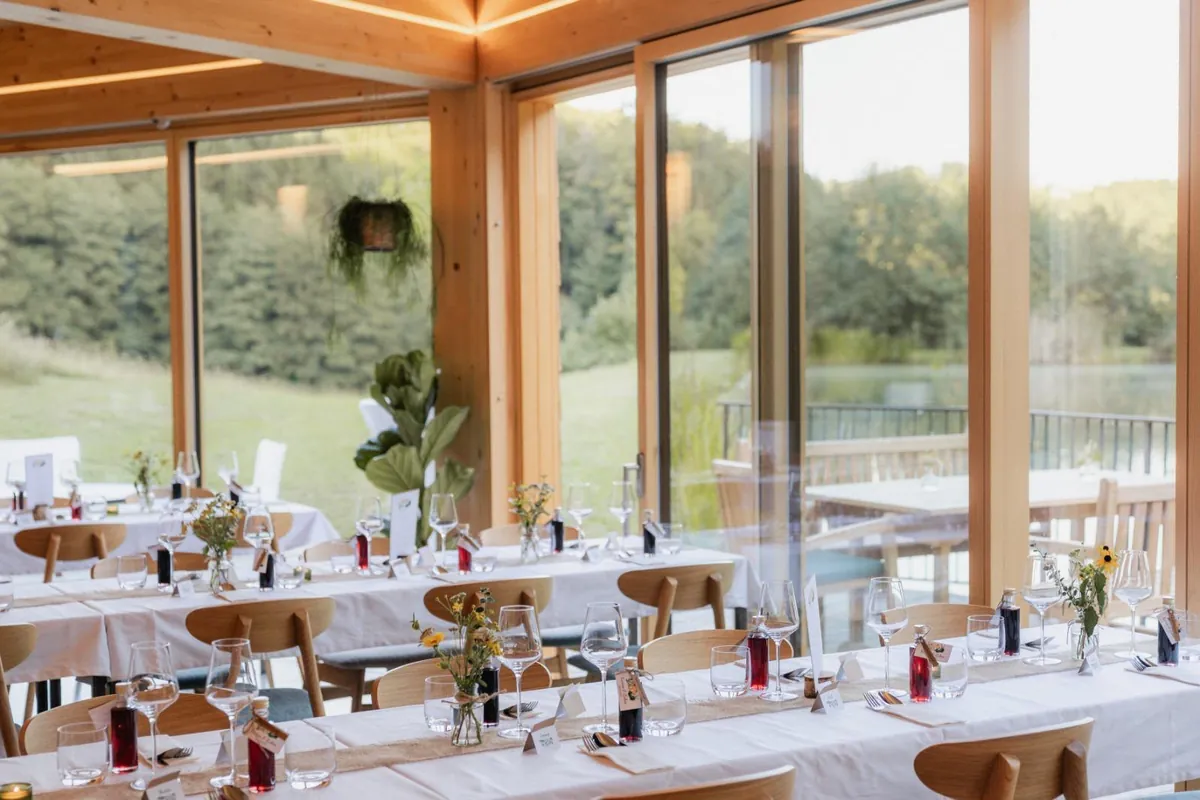 Hochzeitstafeln mit Blumenschmuck im hellen Festsaal mit Holzbalken