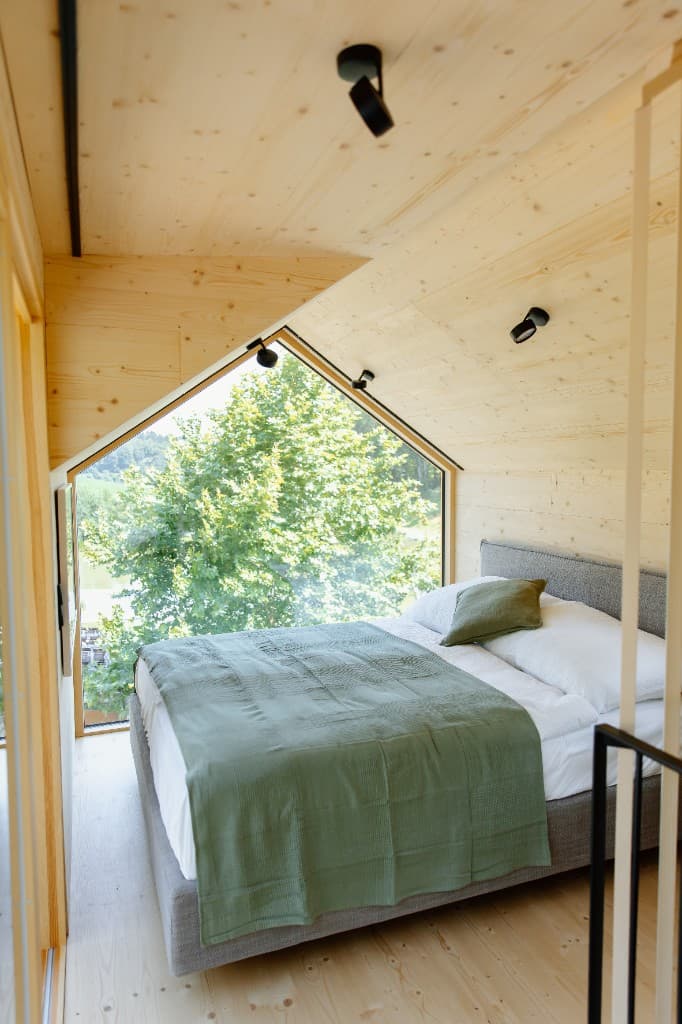 Helles Schlafzimmer im Off Living Chalet mit Holzverkleidung und Blick auf den Wald